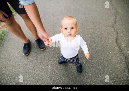 Kleine Junge mit unkenntlich Vater die ersten Schritte in der Natur. Sommer. hoher Blickwinkel betrachten. Stockfoto