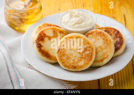Quark Pfannkuchen, hausgemachte, traditionelle ukrainische und russische syrniki mit Honig und saure Sahne serviert. Stockfoto
