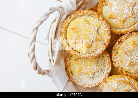 Traditionelle britische Weihnachten Backwaren dessert Hausgemachte mince pies mit Apple Rosinen Nüsse ausfüllen Weidenkorb. golden Mürbteig weiß gepudert. Stockfoto