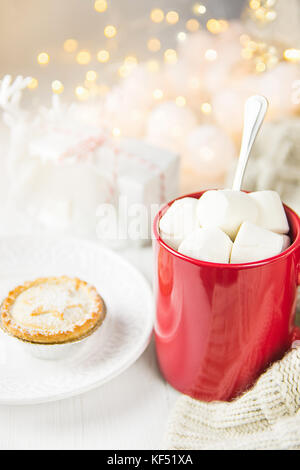 Rot Becher mit heißer Schokolade Kakao trinken und Marshmallows auf pie Hacken. Sekt Girlande Lichter im Hintergrund. strickpullover Geschenkbox. Weiche Paste Stockfoto