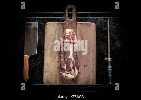 Scheiben Schinken auf einem Holzbrett, ein Messer für Fleisch und ein schleifstein Stockfoto