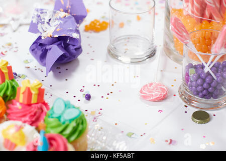 Kindergeburtstag Tisch mit bunten Iced kleine Kuchen und Süßigkeiten, die in Gläsern mit Konfetti bestreut in der Nähe zu sehen. Stockfoto