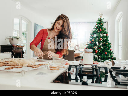 Junge Frau, die in Form von Cookies mit Schneidevorrichtung für Weihnachten. Wohnzimmer mit Weihnachtsbaum im Hintergrund gehalten. Stockfoto