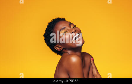 Lachend afrikanischen weibliche Modell mit Make-up gegen den gelben Hintergrund. Studio geschossen von fröhlichen und lebhaften jungen Frau. Stockfoto