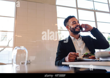 Smiling Young Business mann am Tisch im Restaurant sitzen und essen und Gespräch am Handy. Kaukasische Geschäftsmann im Restaurant telefonieren. Stockfoto