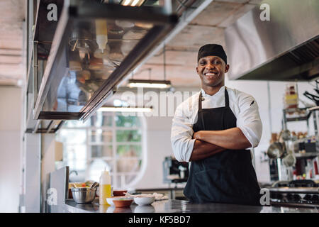 Koch mit seinen Armen stehen im Restaurant Küche gekreuzt. Männliche Koch Schürze tragen, steht die Arbeitsplatte in der Küche und lächelte. Stockfoto