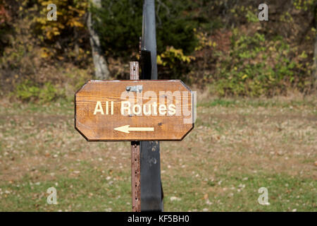 Alle Routen Holz- Schild mit Pfeil, der auf einem ländlichen oder Trail mit Wald Ich den Hintergrund links Stockfoto