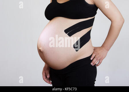 Eine schwangere Frau mit zwei Streifen von Kinesiotaping auf dem Rücken Rückenschmerzen verringern Stockfoto