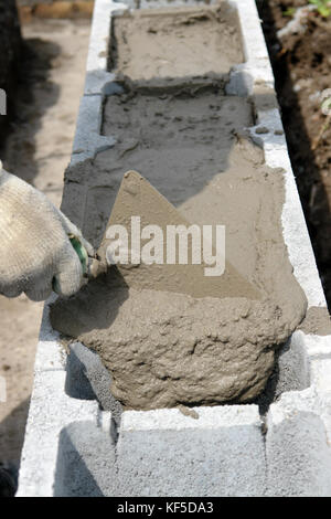 Nahaufnahme von Mason hand Mörtel und Kelle in Beton Schalung Bausteine, Haus Stiftung Stockfoto