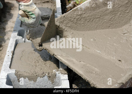 Nahaufnahme von Mason hand Gießen aus Mörtel in Beton Schalung Blocks von Rad - barrow Stockfoto