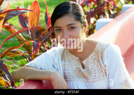 Mexikanische Latin Frau mit ethnischen Kleid im Garten Parkbank sitzen Stockfoto