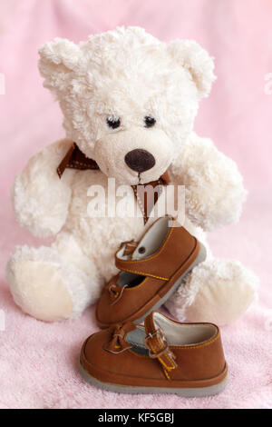 Teddy Bear mit Paar von Mary Jane style Baby Schuhe gegen eine blass rosa Hintergrund. Stockfoto