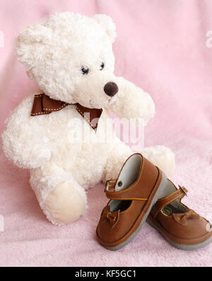 Teddy Bear mit Paar von Mary Jane style Baby Schuhe gegen eine blass rosa Hintergrund. Stockfoto