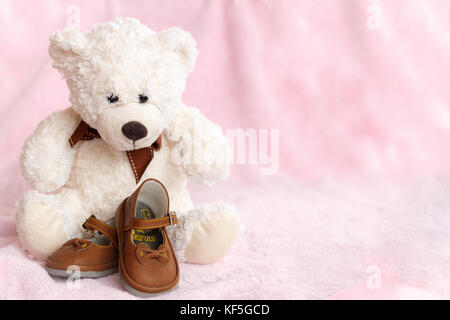 Teddy Bear mit Paar von Mary Jane style Baby Schuhe gegen eine blass rosa Hintergrund. Stockfoto