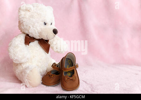 Teddy Bear mit Paar von Mary Jane style Baby Schuhe gegen eine blass rosa Hintergrund. Stockfoto