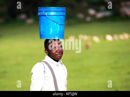 Einem tansanischen Mädchen mit einem Eimer Wasser zurück zu ihrem Haus. Stockfoto