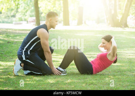 Glückliche junge Frau, Übung mit Hilfe von Mann im Park am Morgen Stockfoto