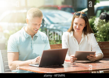 Junge glückliches Paar sitzt auf der Bank mit Laptop und einer Tablette Stockfoto