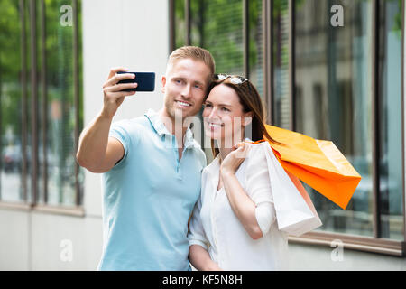 Junge glückliches Paar mit Einkaufstasche unter Bild im Smartphone Stockfoto