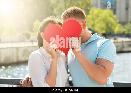 Nahaufnahme des jungen Paares versteckt sich hinter Herzform Stockfoto