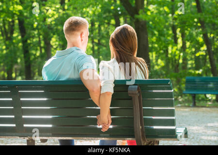 Ansicht der Rückseite des Paar zusammen sitzt auf der Bank und halten sich an den Händen im Park Stockfoto