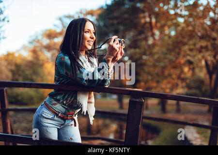 Fotografin Holding professionelle digitale Kamera und Foto auf der Brücke im Herbst City Park. Stockfoto