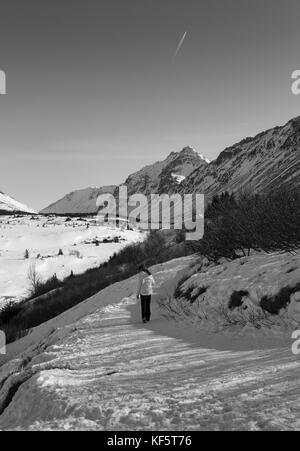 In das große Land. schwarz-weiß-Bild des einsamen Person im Winter Kleidung Wandern auf verschneiten Trail. Bergkette im Hintergrund. Stockfoto