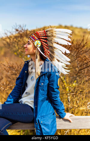 Schöne junge Frau in schwarz gepunkteten weißen Chef Stil Indianer Kopfschmuck während des Sonnenuntergangs Stockfoto