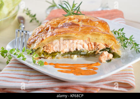 Lachsfilet auf Lauch, in Blätterteig gebacken, serviert mit Kräutern, Sauce und Salat Stockfoto