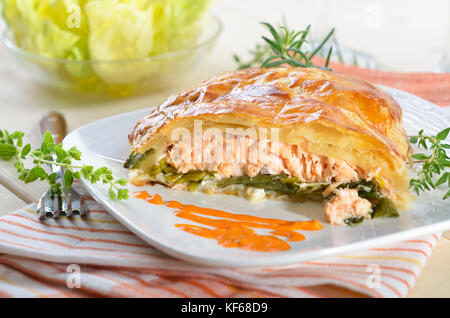 Lachsfilet auf Lauch, in Blätterteig gebacken, serviert mit Kräutern, Sauce und Salat Stockfoto