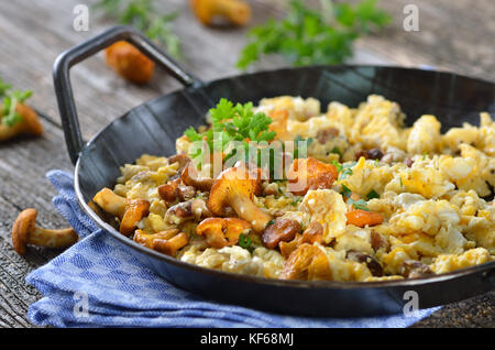 Rührei mit frischen Pfifferlinge in einer Pfanne auf einem alten Holztisch Stockfoto