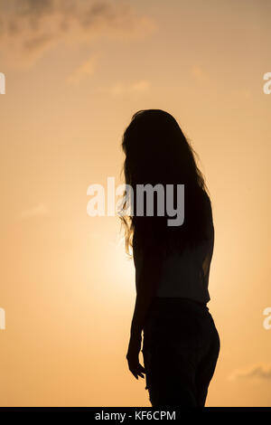 Silhouette einer jungen Frau gegen einen Sonnenuntergang Himmel stehen