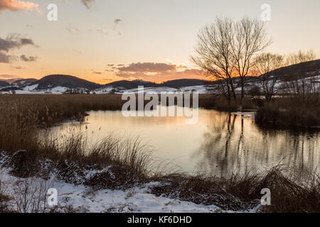 Ein See in colfiorito (Umbrien) im Winter mit Schnee, Bäume auf dem Wasser und einen schönen Himmel mit warmen Sonnenuntergang Farben reflektieren Stockfoto