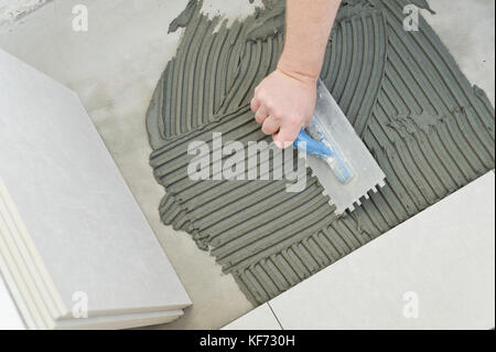 Festlegung der Keramikfliesen. Troweling Mörtel auf Betonboden in der Vorbereitung für die Verlegung von weißen Bodenfliesen. Stockfoto