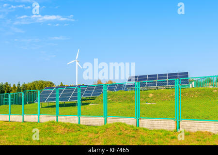 Solaranlagen auf der grünen Wiese mit Windenergieanlage im Hintergrund, Polen Stockfoto