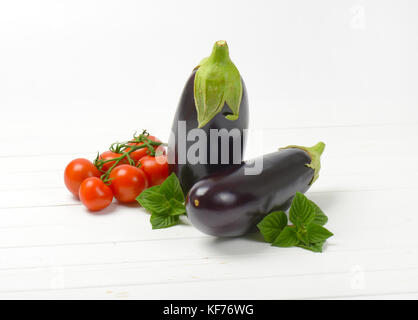 Zwei frische Auberginen, Tomaten und Salbei auf weißem Holz- Hintergrund Stockfoto