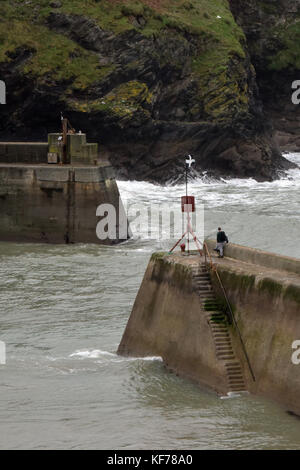 Einer Person, die auf den Hafen Wände oder Dämme am oberen Rand einige Schritte am Eingang zum Hafen von Port Isaac in Cornwall an der Küste von Cornwall. Stockfoto