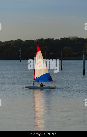 Kleine Jolle mit weißen, roten und blauen Segeln, günstig auf einem Ponton in Chichester Harbour. Stockfoto