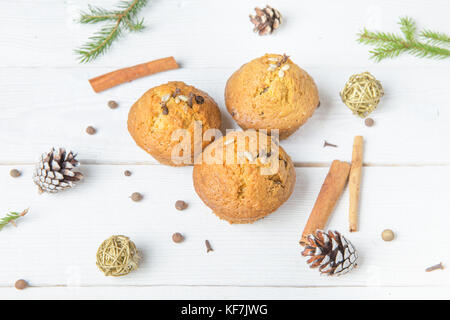 Weihnachten Komposition. Weihnachten Cupcakes mit Gewürze Gewürznelken, Samen und Nüsse, Notizblock, Stift, Tannenzapfen auf hölzernen weißen Hintergrund. Flach, Ansicht von oben. Stockfoto