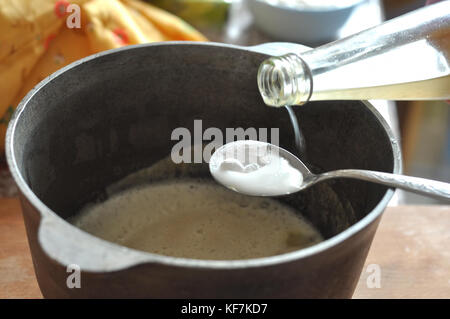 Prozess der Abschrecken der Natron mit dem Essig in einem Löffel über eine gusseiserne Schüssel mit dem Teig. close-up Bild. Prozess des Kochens. Stockfoto