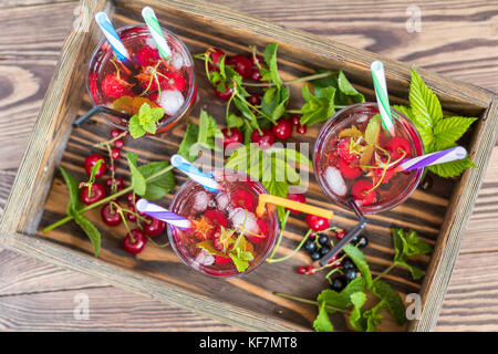 Drei Gläser erfrischenden Drink gewürzt mit frischem Obst im Holzkasten von Obst umgeben. top View. Holz- Hintergrund Stockfoto