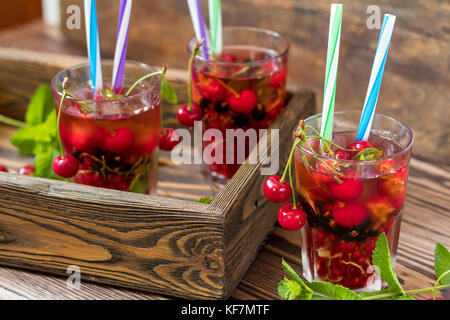 Drei Gläser erfrischenden Drink gewürzt mit frischem Obst im Holzkasten von Obst umgeben. Holz- Hintergrund Stockfoto