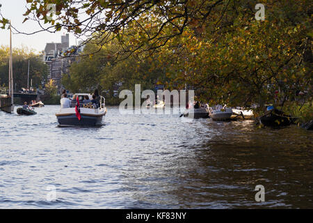 Boote segeln auf Amsterdam Canal mit Bäumen an der Seite an einem sonnigen Herbsttag. Stockfoto