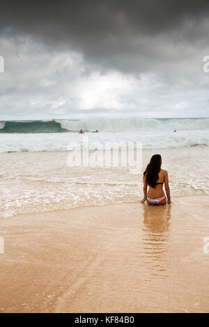 Usa, Oahu, Hawaii, Logan garcia sitzt am Strand am Rand der Brandung am Pipeline Beach an der Nordküste Stockfoto