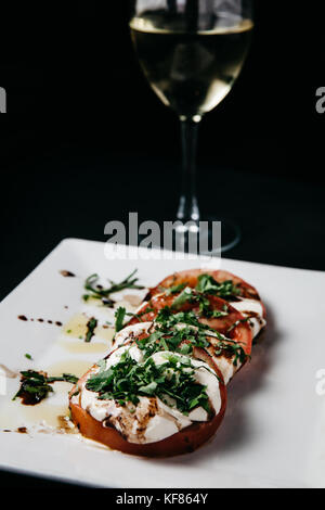 Frische italienische Caprese Salat mit Mozzarella, Tomaten und Basilikum auf einer weißen Platte und schwarzen Hintergrund Stockfoto