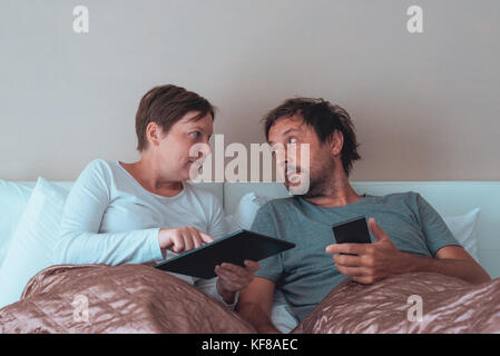 Ernsthafte Paar, Mann und Frau im Schlafzimmer über elektronische Geräte Stockfoto