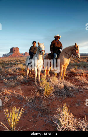 Usa; Arizona; Monument Valley, Navajo Tribal Park, ein Navajo Mann und sein Sohn reiten mit Mitchell Butte und Mitchell Mesa in der Ferne Stockfoto