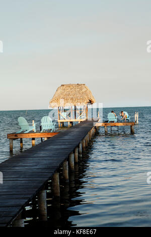 Belize, Caye Caulker, Touristen auf einem Pier entspannen am Wasser bei Sonnenuntergang Stockfoto