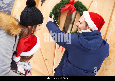 Mann hängen die Weihnachten Kranz an der Tür Stockfoto