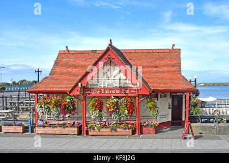 Sommerblumen in Pflanzmaschinen und hängende Körbe vor dem Lakeside Inn an der Promenade neben dem Marine Lake in Southport einst kleinster Pub in England Stockfoto